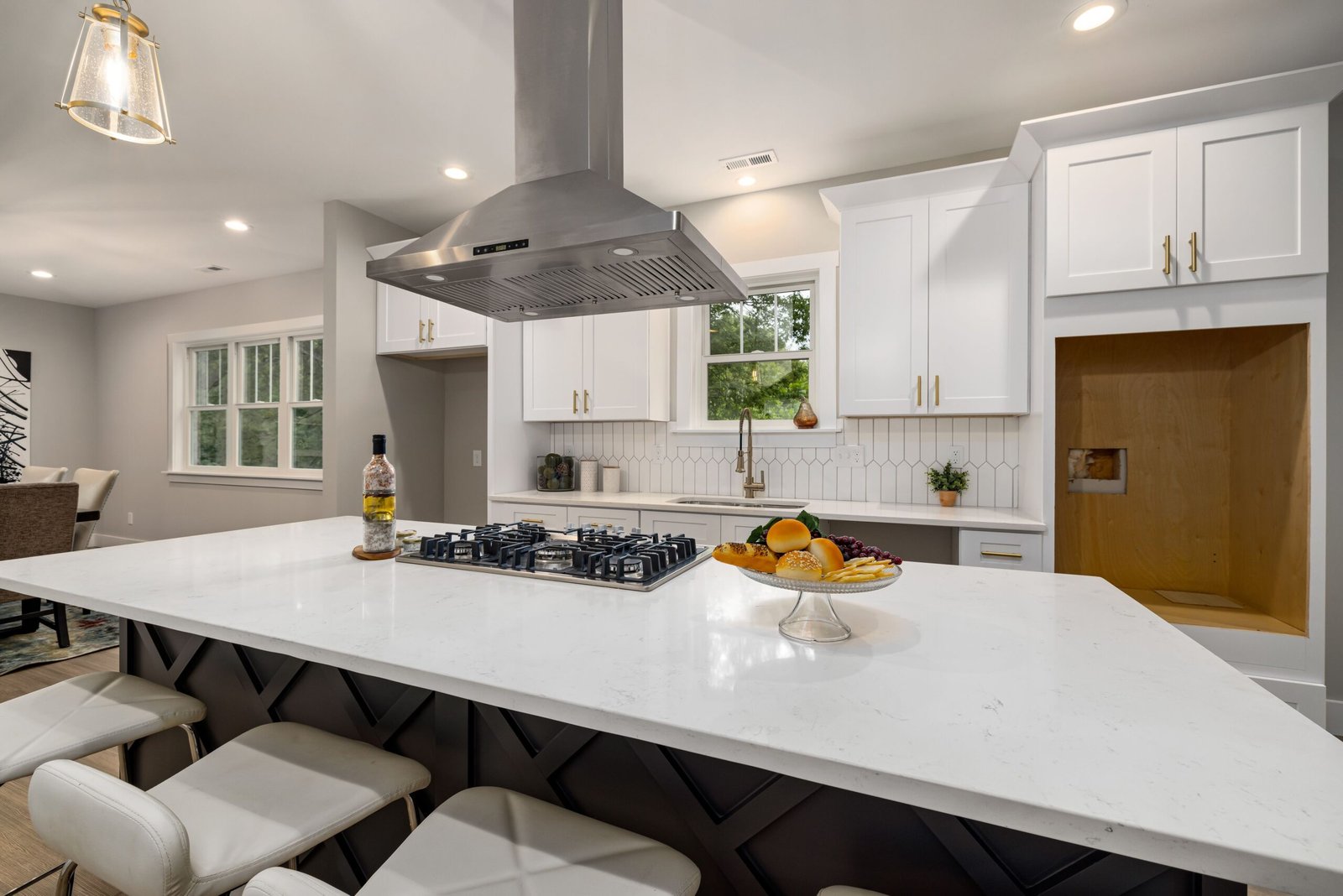 Bright remodeled kitchen with white cabinets, a large island with a gas cooktop, a stainless steel range hood, and seating.