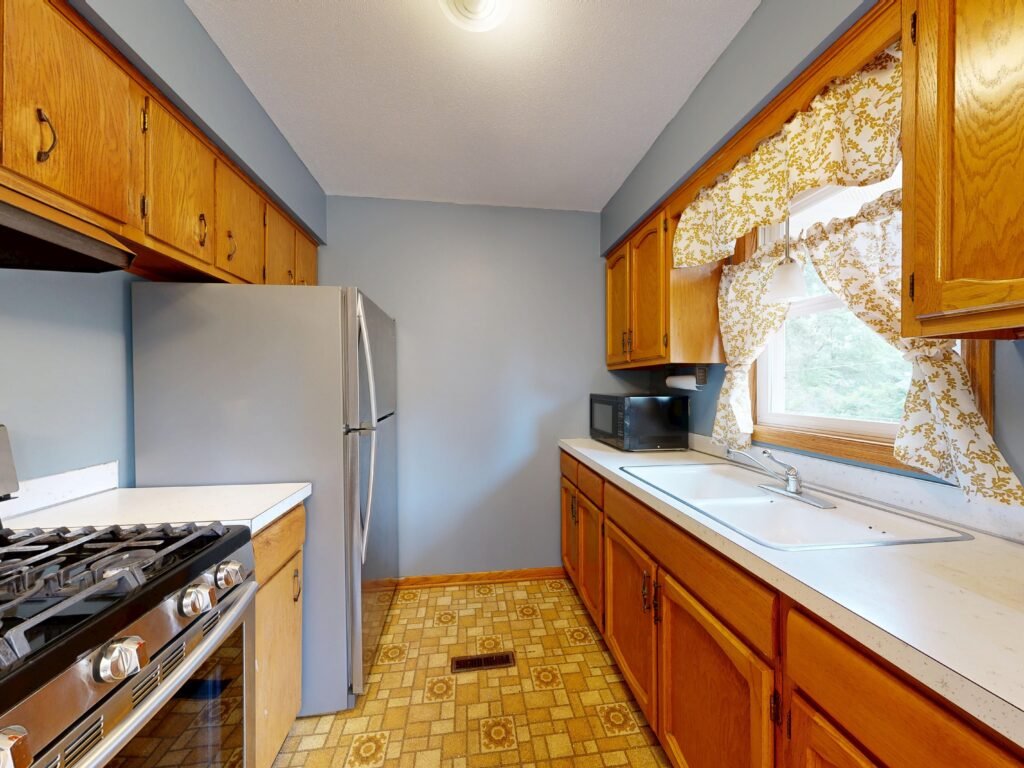 Small galley kitchen with wood cabinets, white countertops, stainless steel appliances, and patterned flooring.